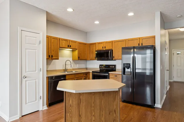 a kitchen with stainless steel appliances a refrigerator a stove a sink a center island and couches with wooden floor