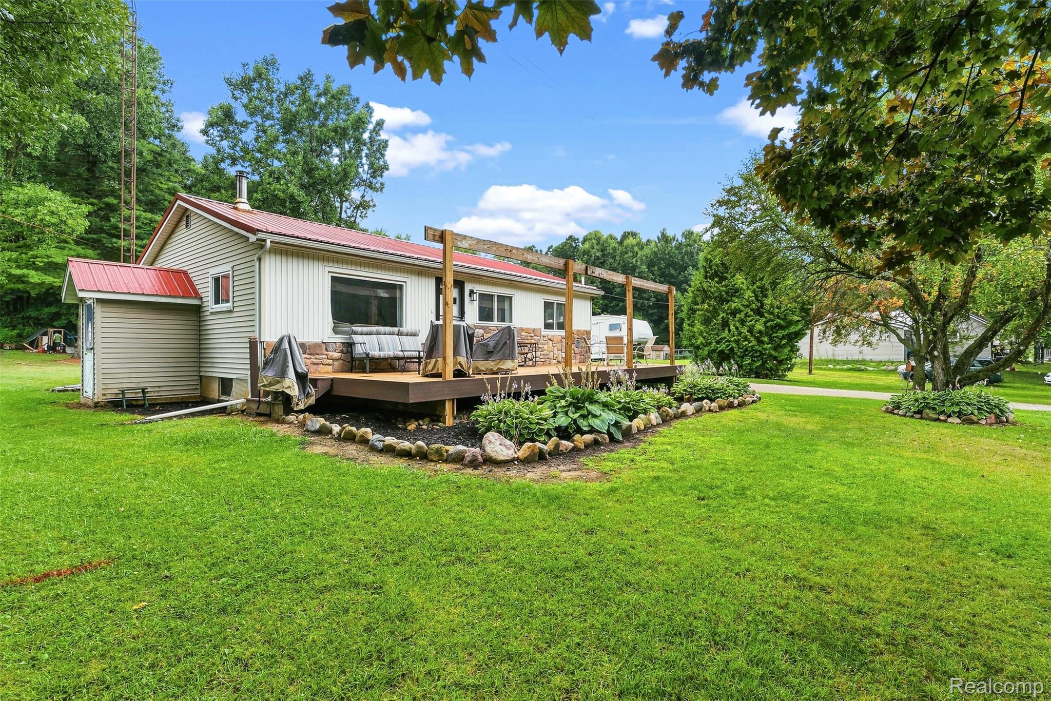 3319 Valentine Road Lapeer, MI 48446 - Photo 37 of 39 Wood-look deck with a pergola frame, stone veneer accent, and red metal roofing