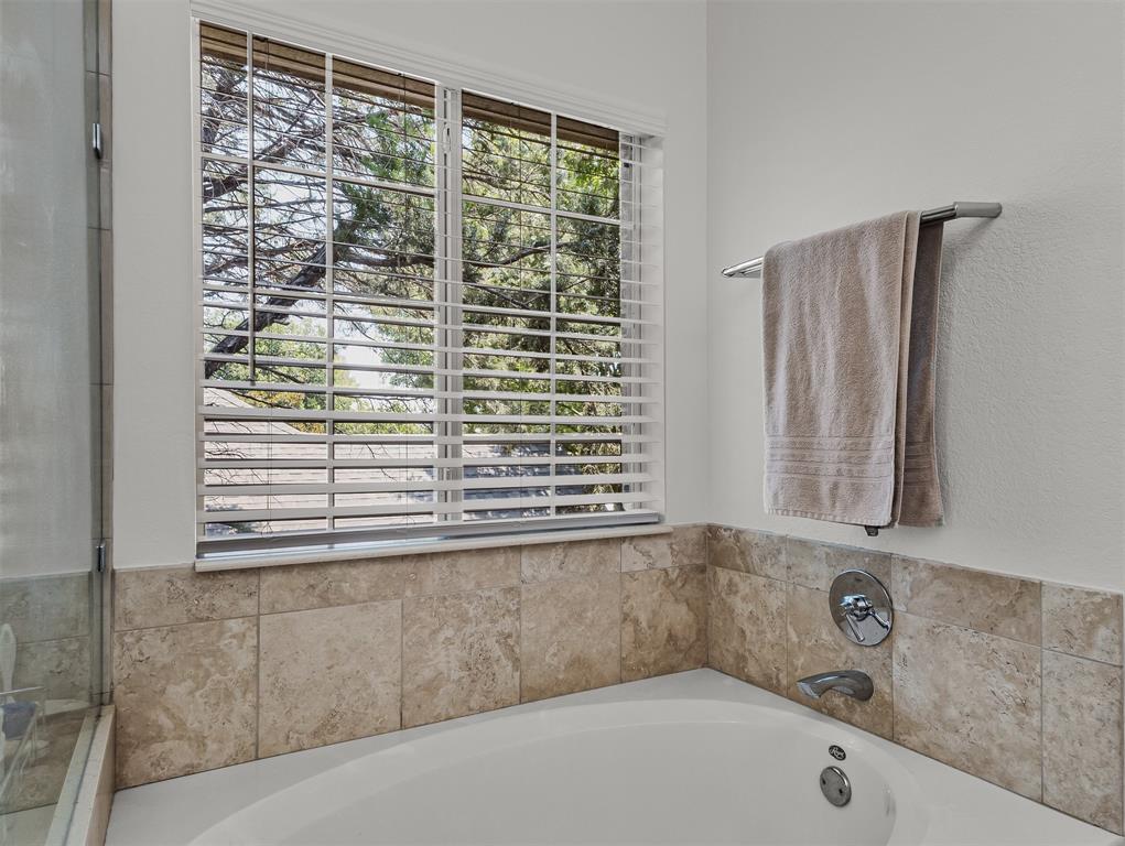 9301 Nottingham Court Rowlett, TX 75088 - Photo 17 of 39 Soaking tub featuring stone-look tile surround, chrome fixtures, and a large window with white blinds