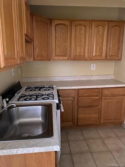 199 Hoover Road, Unit 2F Yonkers, NY 10710 - Photo 10 of 16 Kitchen featuring light countertops, gas range oven, light tile patterned flooring, and brown cabinets