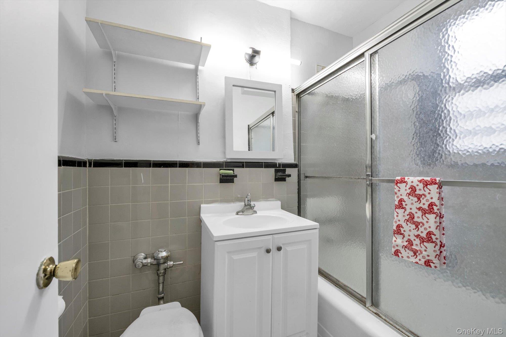 42-25 80th Street, Unit 3D Queens, NY 11373 - Photo 15 of 17 Bathroom featuring tile walls, vanity, bath / shower combo with glass door, and wainscoting