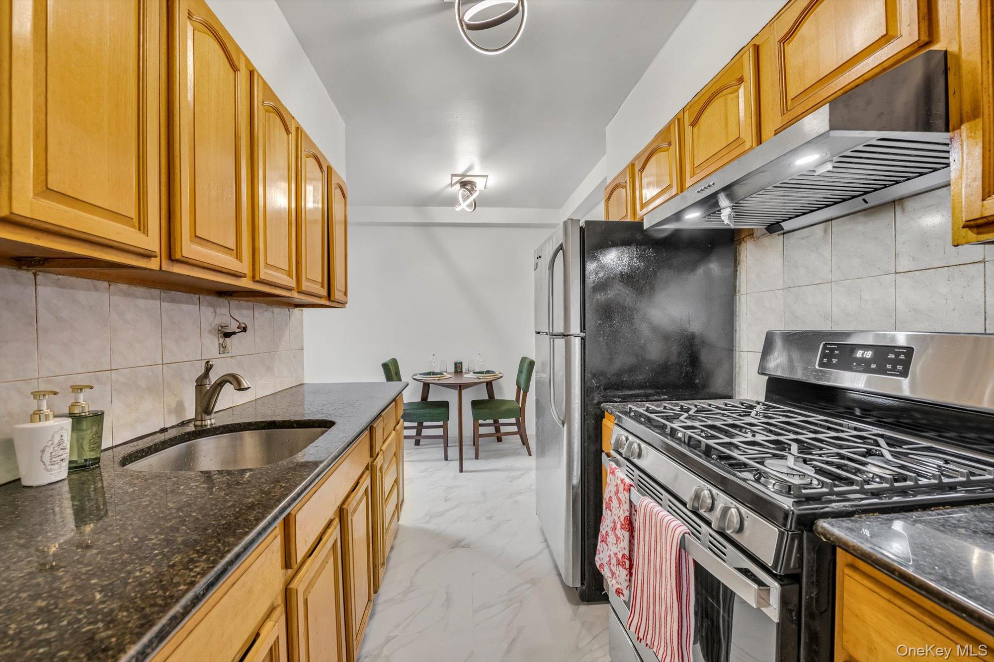 42-25 80th Street, Unit 3D Queens, NY 11373 - Photo 9 of 17 Kitchen with appliances with stainless steel finishes, dark stone countertops, decorative backsplash, under cabinet range hood, and light marble finish flooring