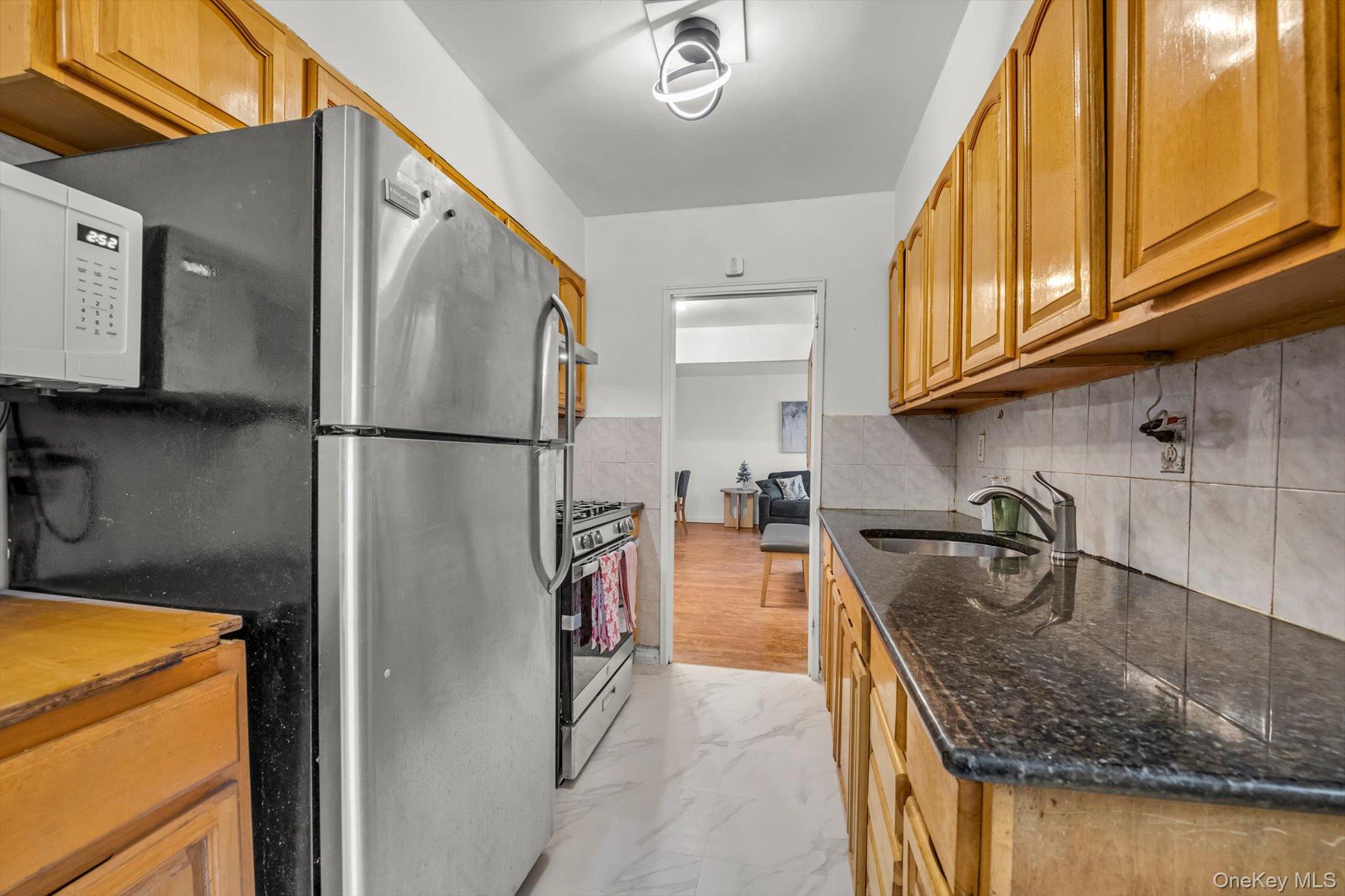 42-25 80th Street, Unit 3D Queens, NY 11373 - Photo 10 of 17 Kitchen with light marble finish floors, stainless steel appliances, dark stone countertops, brown cabinets, and backsplash