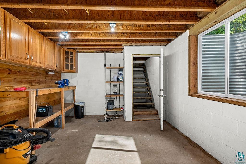 5466 Jean Duluth Road Duluth, MN 55803 - Photo 17 of 34 Unfinished basement space featuring a built-in workbench with wood cabinetry, exposed ceiling joists, concrete block walls, and a window well with a window