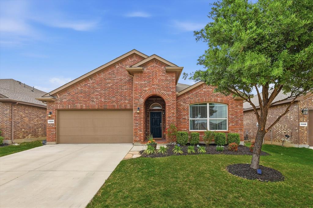 This property features a brick exterior, an attached garage, a well-maintained lawn, and a mature tree in the front yard