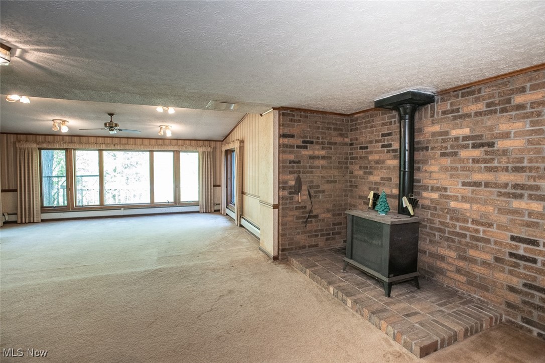 41180 Butternut Ridge Road Elyria, OH 44035 - Photo 46 of 50 Unfurnished living room featuring carpet floors, a wood stove, a textured ceiling, ceiling fan, and a baseboard radiator