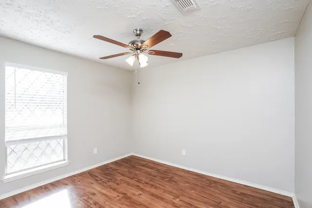 an empty room with wooden floor fan and windows