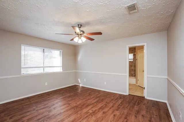 an empty room with wooden floor chandelier fan and windows