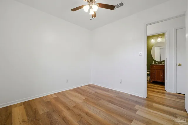 an empty room with a chandelier fan and wooden floor