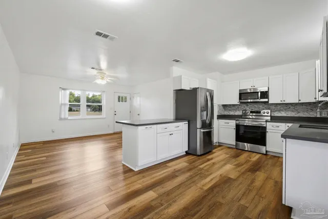 a kitchen with granite countertop a refrigerator oven a sink dishwasher and white cabinets with wooden floor