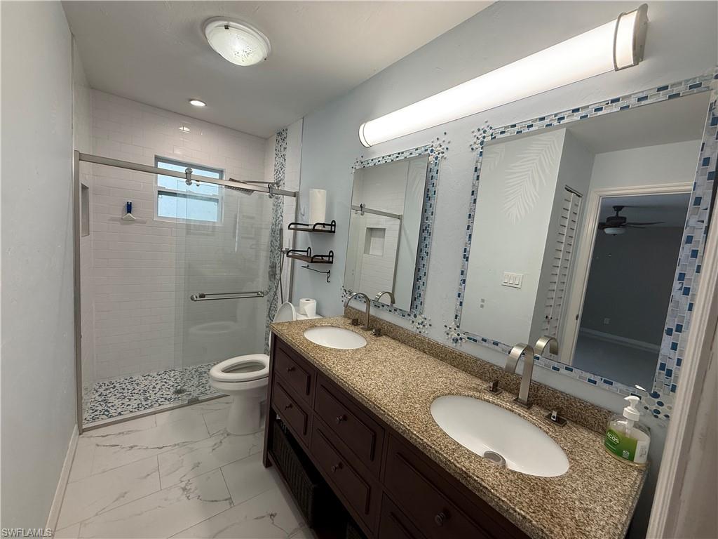 410 6th Street Northeast Naples, FL 34120 - Photo 28 of 32 Master bath with double vanity, granite counters, light marble flooring, and shower with glass door.