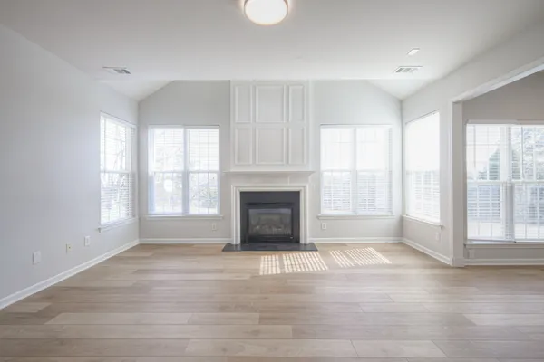 an empty room with wooden floor fireplace and windows