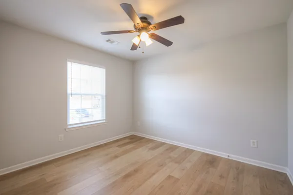 an empty room with wooden floor fan and windows
