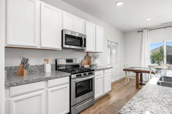 a kitchen with stainless steel appliances granite countertop a stove a sink dishwasher and a microwave oven with white cabinets
