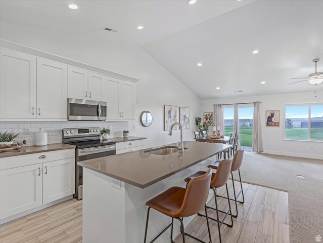 1278 South Grace Way Layton, UT 84041 - Photo 6 of 23 Modern kitchen featuring white shaker cabinetry, stainless steel appliances, a subway tile backsplash, and a large island with an undermount sink