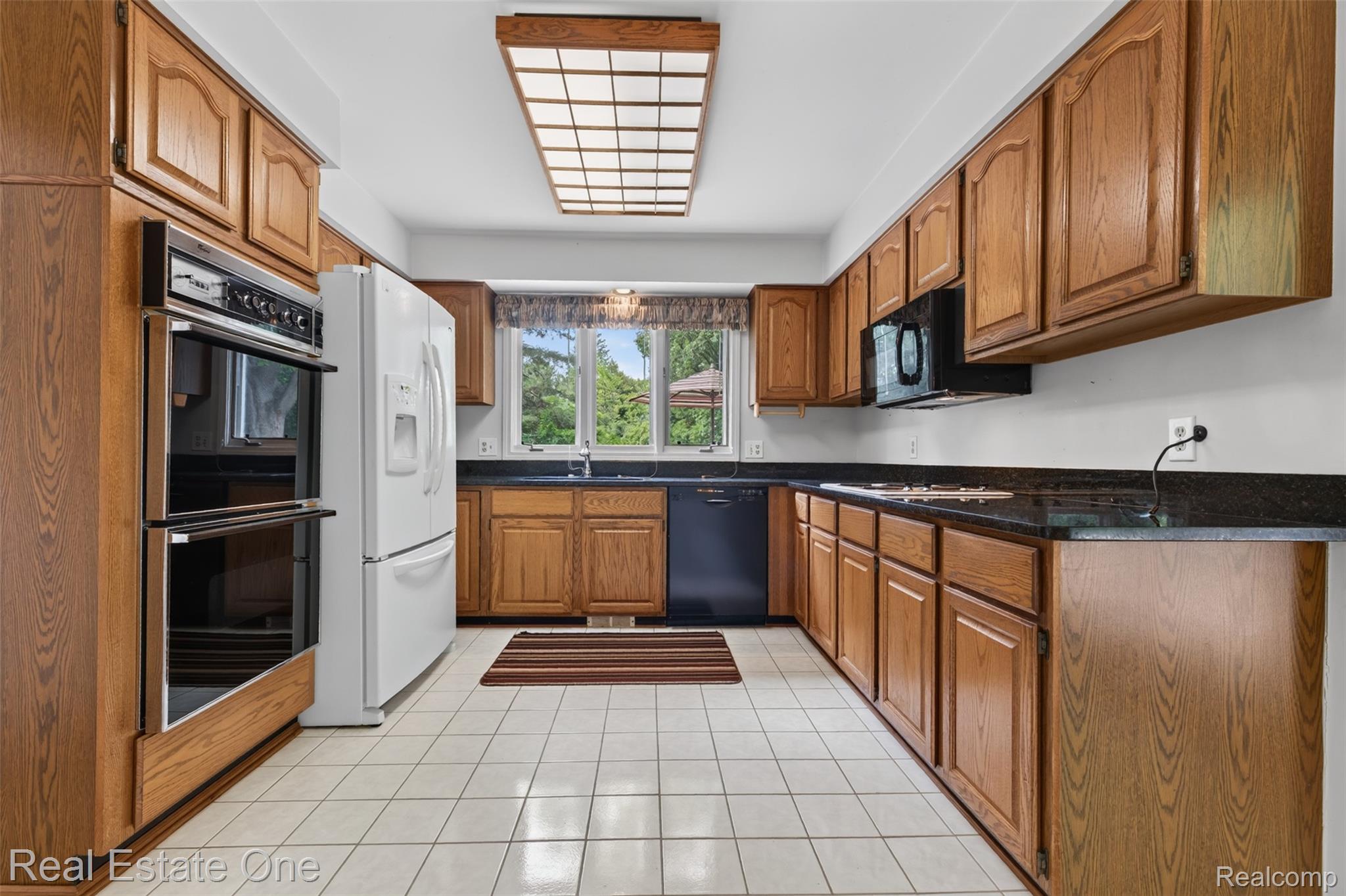 3400 Wedgewood Drive Rochester, MI 48306 - Photo 13 of 49 Kitchen featuring wood-finish cabinetry, black countertops, white tile flooring, and integrated double ovens