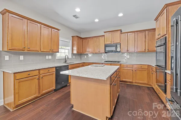 a kitchen with granite countertop wooden cabinets a sink and dishwasher a stove with wooden floor