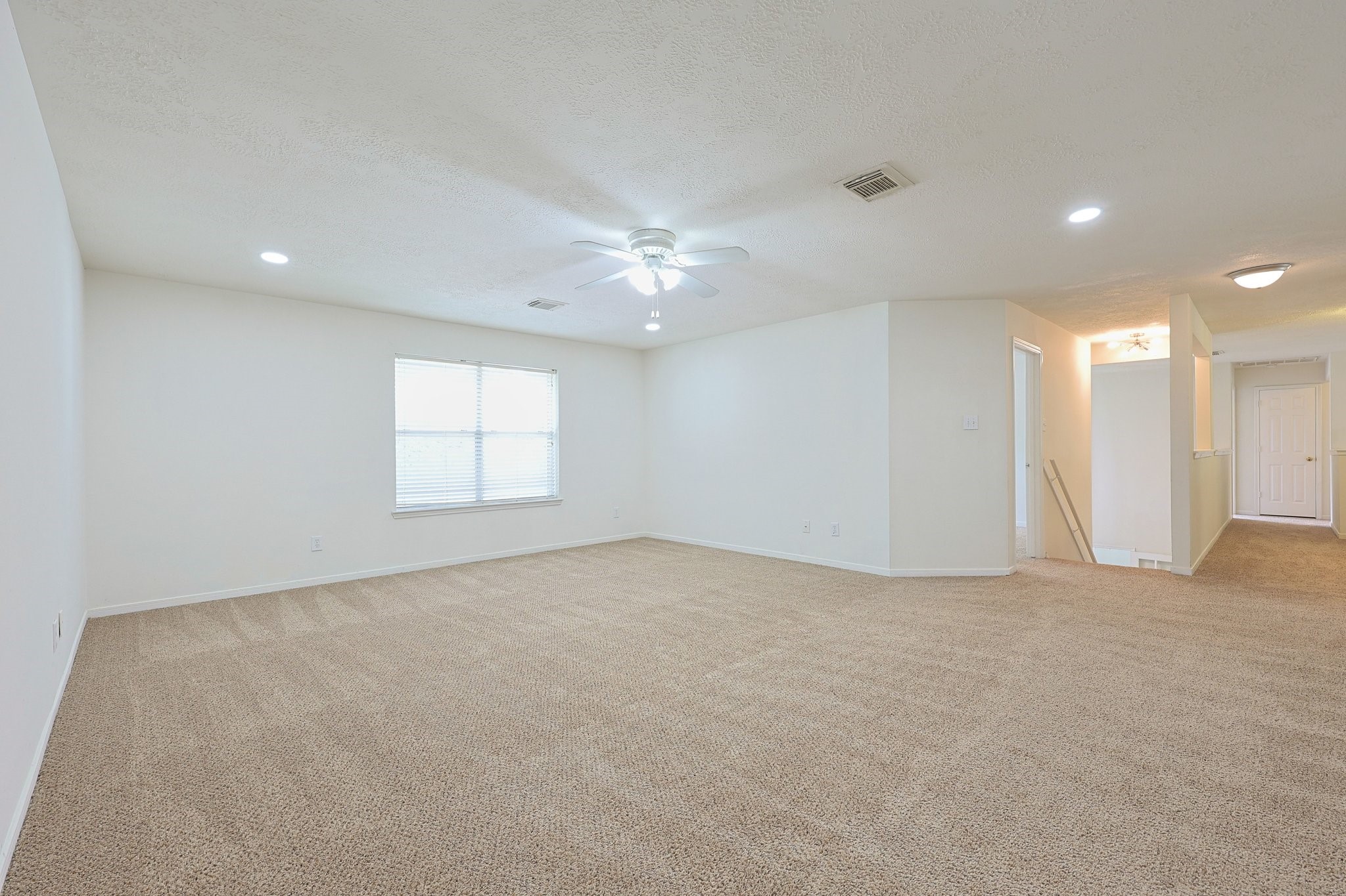 23019 Eastgate Village Drive Spring, TX 77373 - Photo 29 of 46 Spacious living area with neutral tones, featuring carpeted flooring, recessed lighting, and a ceiling fan. Natural light fills the room through a large window, creating an inviting atmosphere.