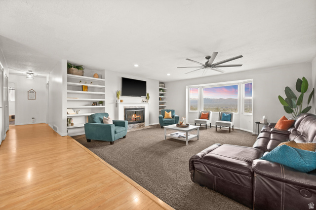 9750 Indian Ridge Drive Sandy, UT 84092 - Photo 10 of 40 Living room with a ceiling fan, a fireplace with flush hearth, wood finished floors, recessed lighting, and built in shelves