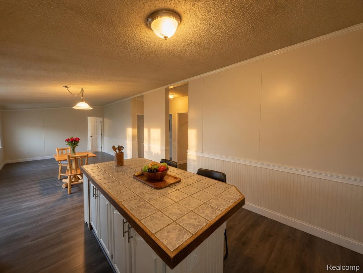 6988 McKean Road Ypsilanti, MI 48197 - Photo 7 of 31 Kitchen featuring tile counters, dark wood finished floors, a center island, white cabinetry, and a textured ceiling