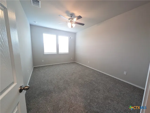 an empty room with chandelier fan and windows