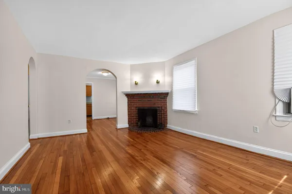 a view of an empty room with wooden floor fireplace and a window