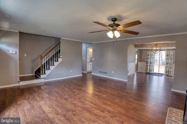 a view of an empty room with wooden floor and a ceiling fan