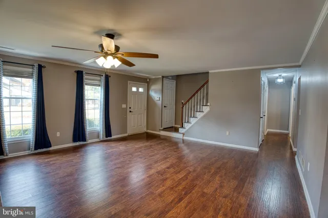 a view of an empty room with wooden floor and a ceiling fan