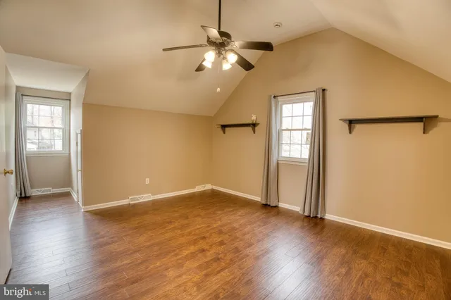 an empty room with wooden floor chandelier fan and windows