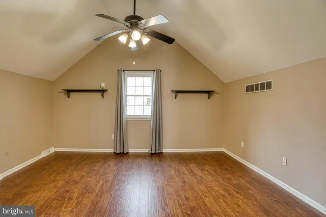 an empty room with wooden floor chandelier fan and windows