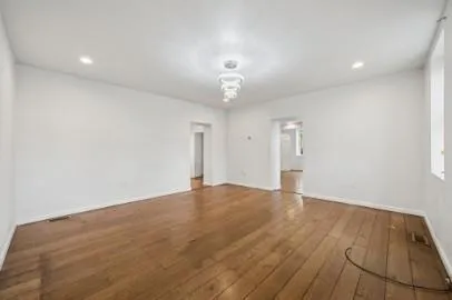 a view of an empty room with wooden floor and a ceiling fan