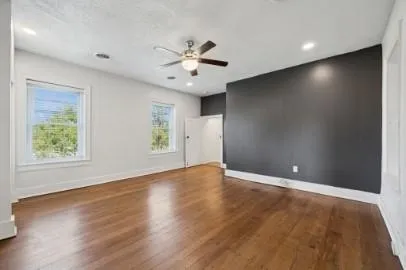 an empty room with wooden floor chandelier fan and windows