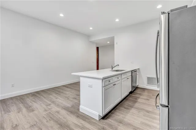 a large white kitchen with sink a stove a refrigerator and white cabinets with wooden floor