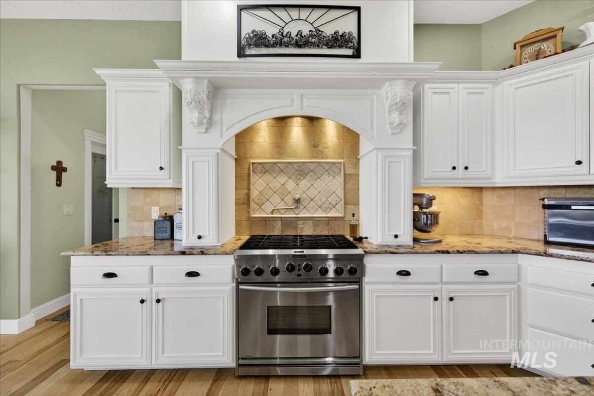 414 East Shafer View Drive Meridian, ID 83642 - Photo 10 of 50 Gourmet kitchen featuring a professional-grade six burner stainless steel range, custom range hood with ornate corbels & built-in spice racks, pot filler, white cabinetry, granite countertops, and a tiled backsplash. This is a COOK'S Kitchen!