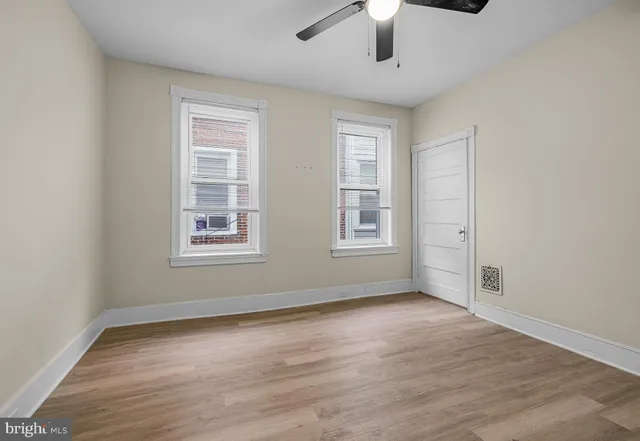 an empty room with wooden floor chandelier fan and windows