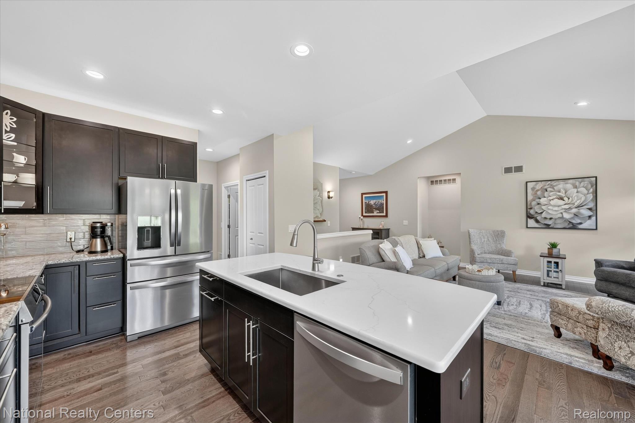 740 North Mill Street South Lyon, MI 48178 - Photo 20 of 56 Open-concept kitchen featuring dark wood cabinetry, stainless steel appliances, a white quartz island with an undermount sink, and wood-finish flooring