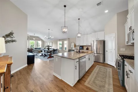 a view of a dining room and livingroom with furniture wooden floor a rug a painting and a chandelier