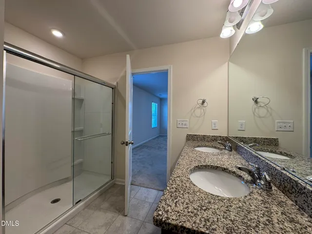 a en suite bathroom with a granite countertop sink a mirror and shower