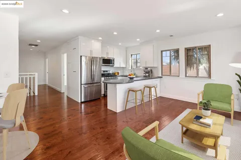 a living room with stainless steel appliances furniture wooden floor and a kitchen view