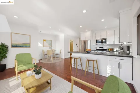 a living room with stainless steel appliances furniture a rug and a kitchen view