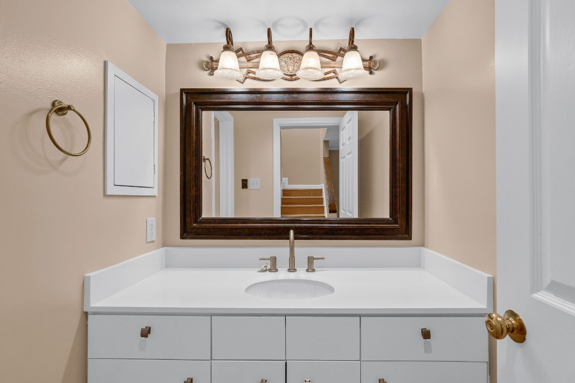 5084 Augusta Street Houston, TX 77007 - Photo 24 of 43 Guest bathroom features a modern white vanity with a sleek countertop/sink. Large framed mirror and stylish lighting fixtures above. The neutral wall color complements the gold towel ring and hardware, creating a warm and inviting atmosphere.