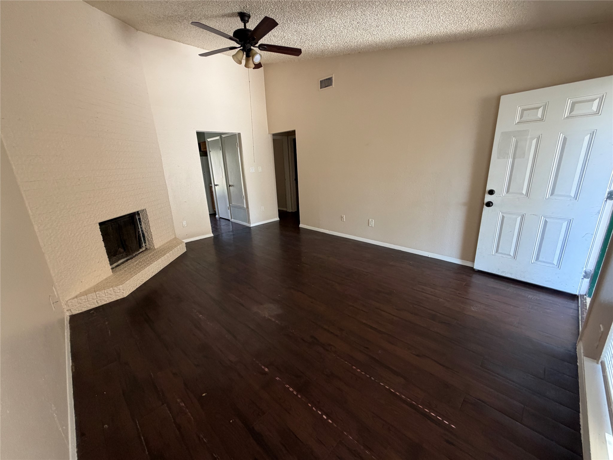 4702 Rocking Chair Road Austin, TX 78744 - Photo 13 of 28 Unfurnished living room featuring a brick fireplace, dark wood-style flooring, ceiling fan, and a high textured ceiling