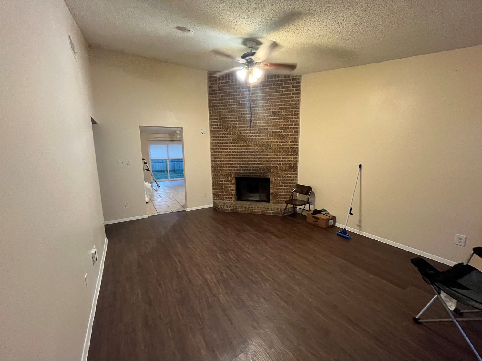 4702 Rocking Chair Road Austin, TX 78744 - Photo 22 of 28 Unfurnished living room featuring dark wood finished floors, a textured ceiling, ceiling fan, and a fireplace