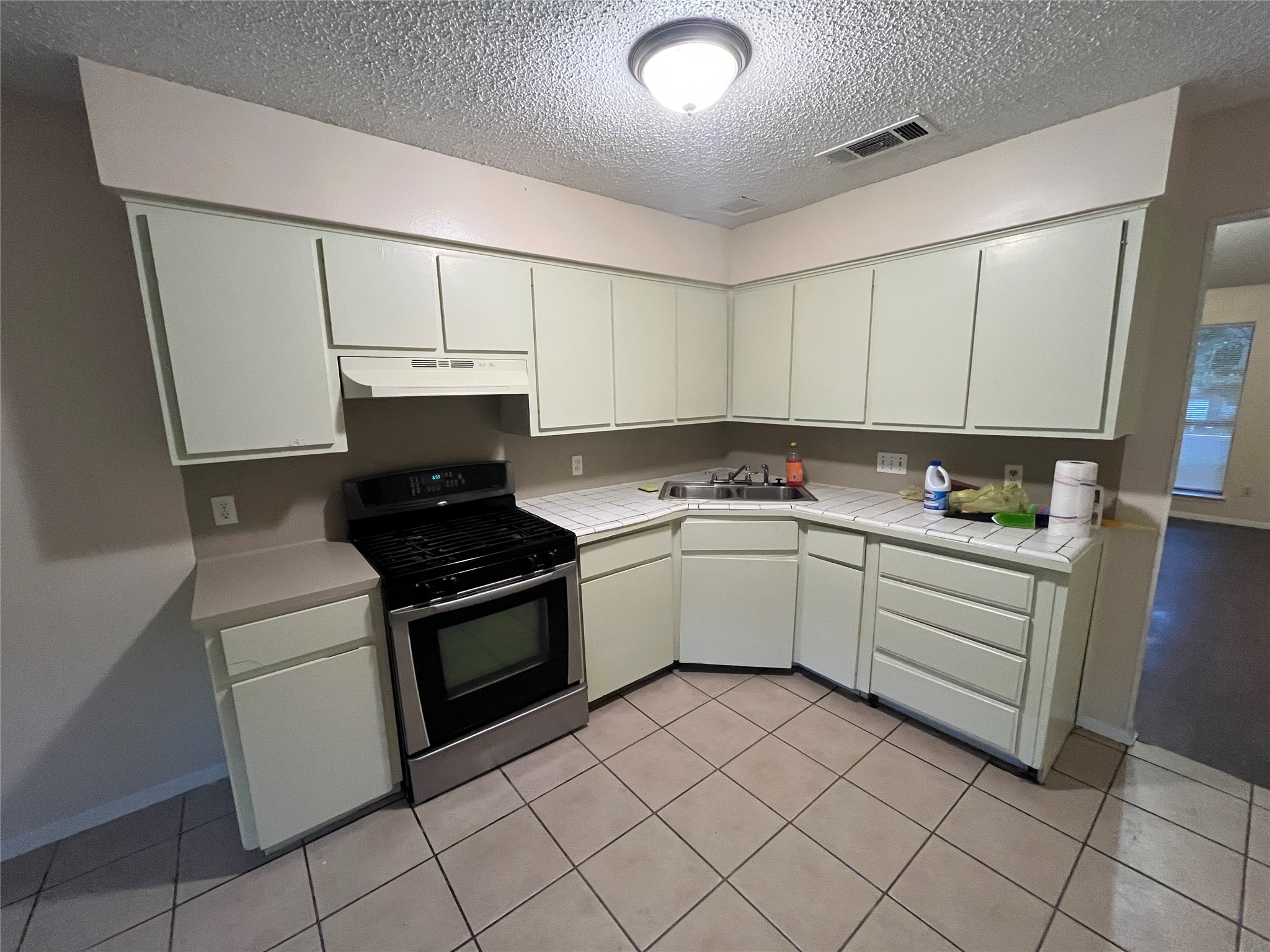 4702 Rocking Chair Road Austin, TX 78744 - Photo 24 of 28 Kitchen with gas stove, tile countertops, a textured ceiling, white cabinetry, and light tile patterned floors