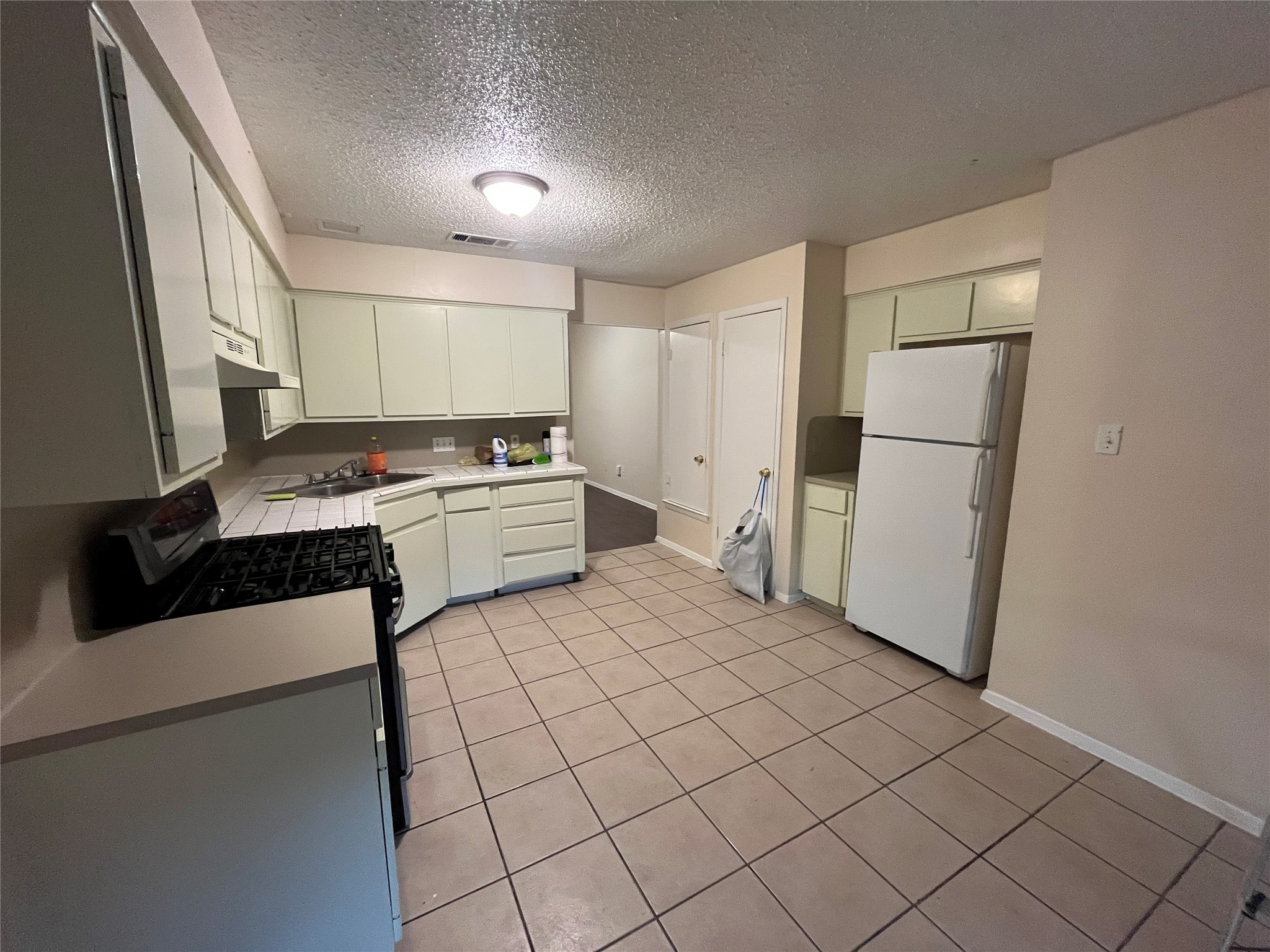 4702 Rocking Chair Road Austin, TX 78744 - Photo 25 of 28 Kitchen with freestanding refrigerator, black range with gas stovetop, tile counters, a textured ceiling, and light tile patterned floors