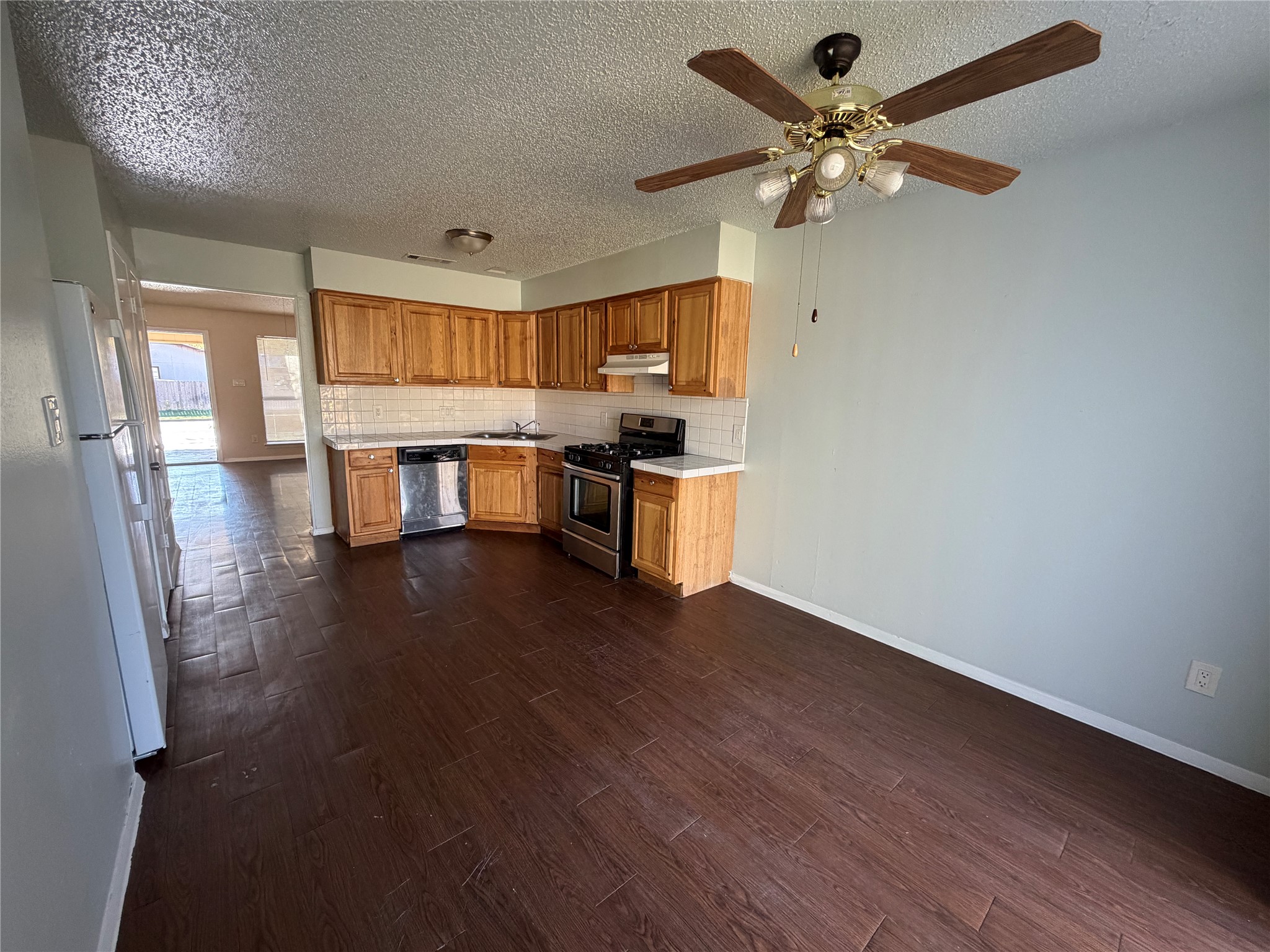 4702 Rocking Chair Road Austin, TX 78744 - Photo 7 of 28 Kitchen with light countertops, stainless steel appliances, dark wood-style floors, decorative backsplash, and a textured ceiling