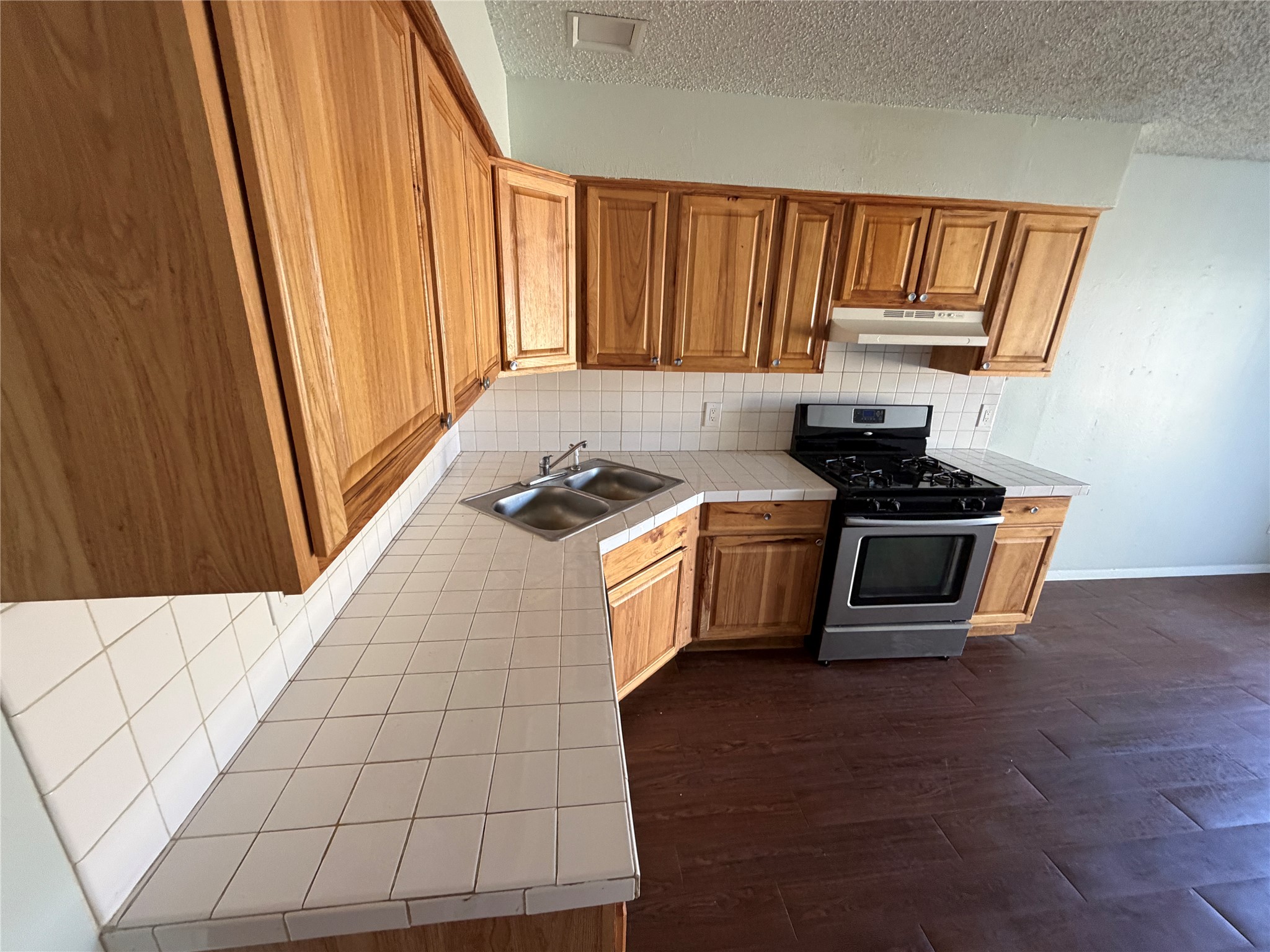4702 Rocking Chair Road Austin, TX 78744 - Photo 8 of 28 Kitchen with tile counters, stainless steel range with gas stovetop, wood finish cabinetry, dark wood finished floors, and a textured ceiling