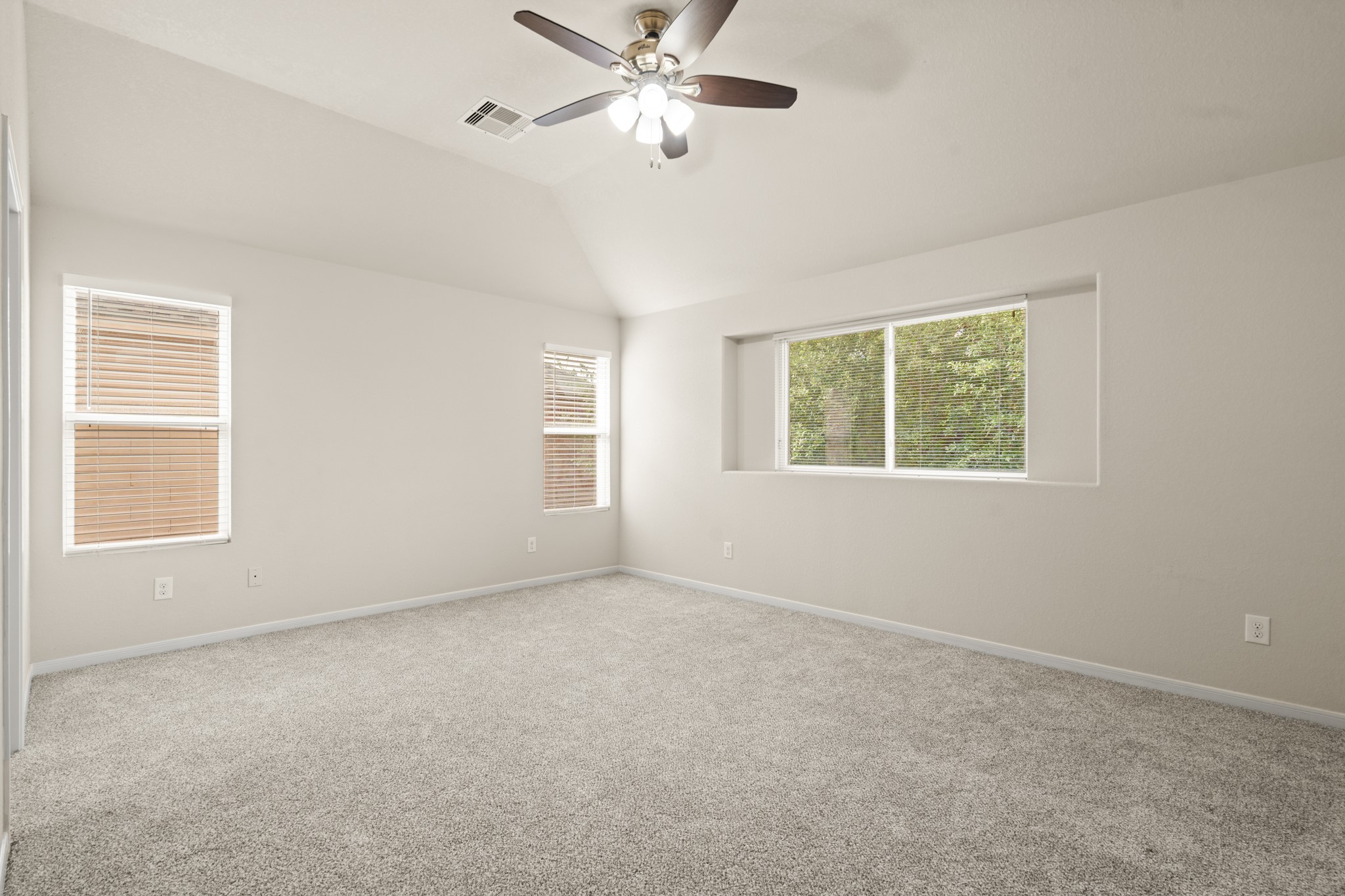 3118 Winchester Rnch Trail Katy, TX 77493 - Photo 13 of 22 This wide-angle view of the primary bedroom showcases the full scale of the space, with plush carpet, multiple windows bringing in beautiful natural light and lush tree views, a ceiling fan, and a vaulted ceiling — a serene and spacious sanctuary for the homeowner to enjoy.