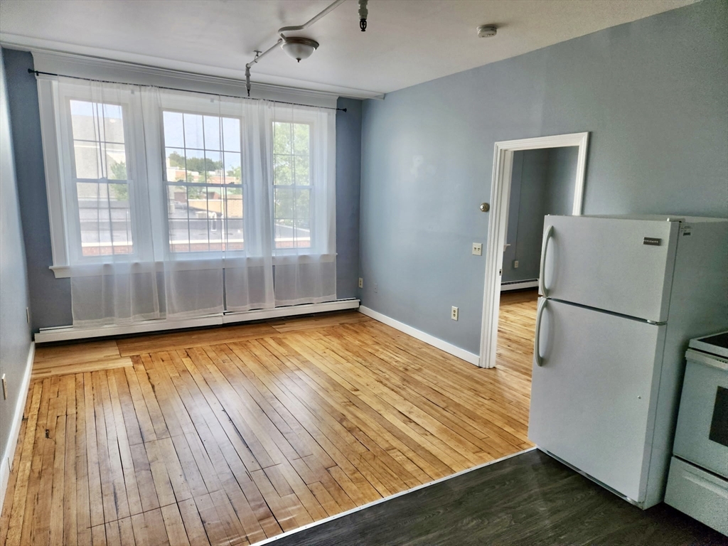 a view of empty room with wooden floor and a kitchen