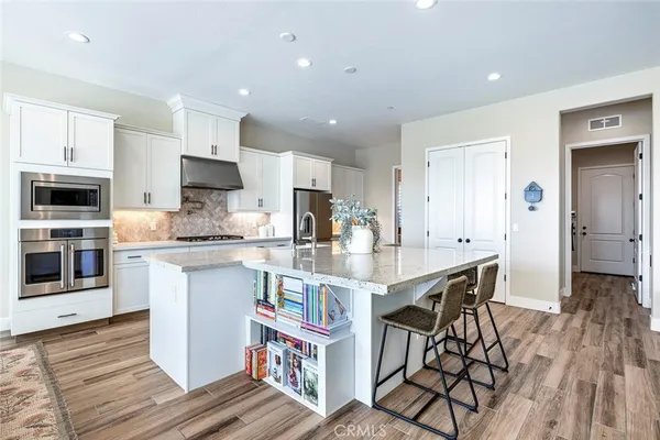 a kitchen with stainless steel appliances granite countertop a stove top oven a sink dishwasher and a refrigerator with wooden floor